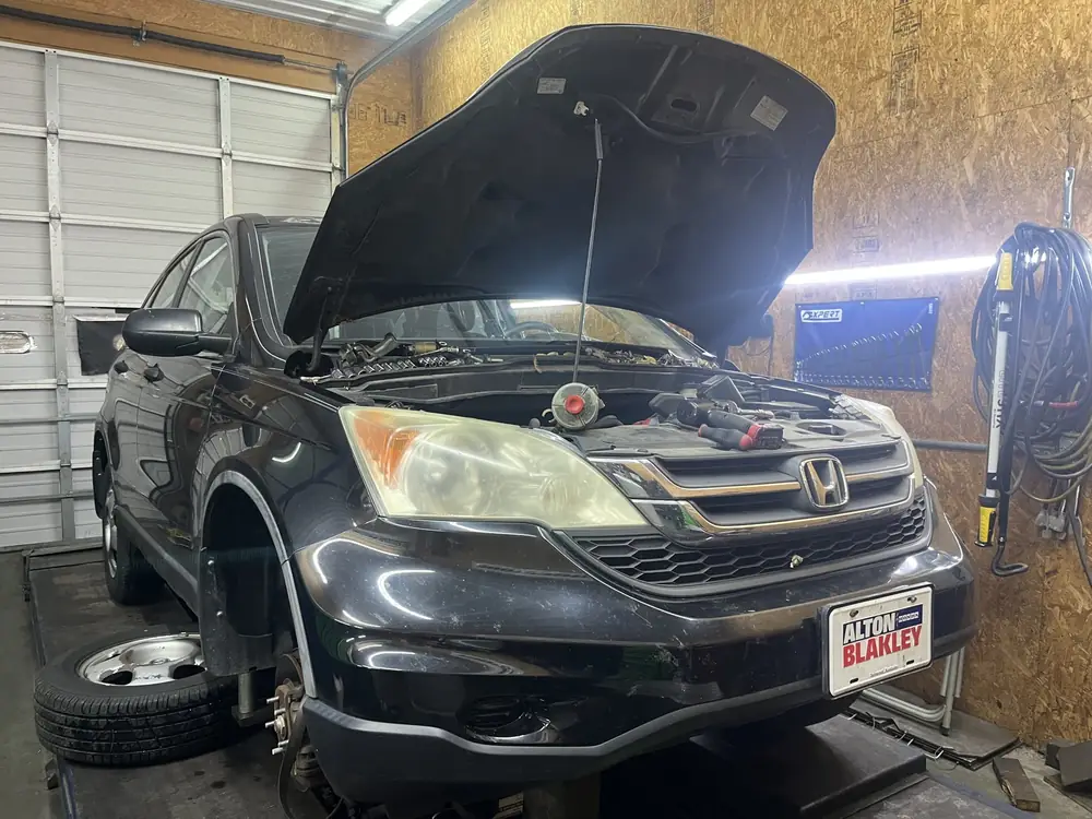 Black Honda CR-V in the bay with the hood open and a wheel off