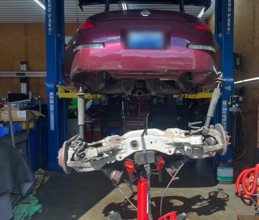 Burgundy Nissan 350Z on the lift with the rear subframe and suspension lowered on a jack